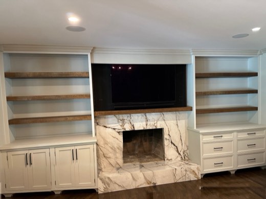 White built-ins with walnut floating shelves around a marble fireplace